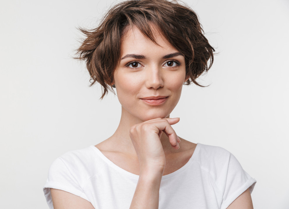 Portrait of cute woman with short brown hair in basic t-shirt looking at camera while standing isolated over white background