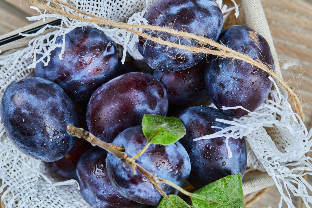 Garden plums in a basket on a wooden table, close up. High quality photo